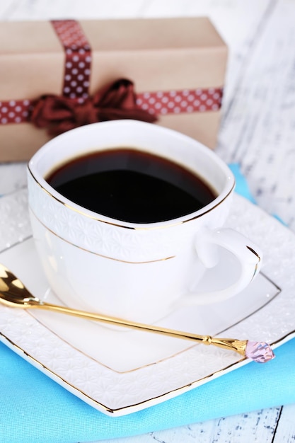 Cup of coffee and gift on wooden table close-up