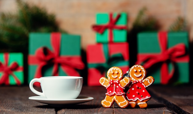 Cup of coffee and gingerbread man and woman next to Christmas gifts on wooden table