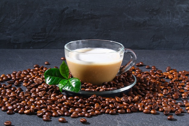 Cup of coffee on a gray table with coffee beans and coffee leaves