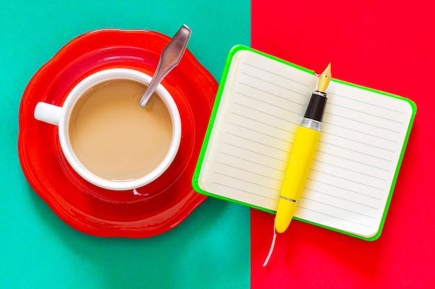 緑のノートと黄色の万年筆の横にある一杯のコーヒー。朝食からメモを取ったり、一日を整理したりする準備ができています。