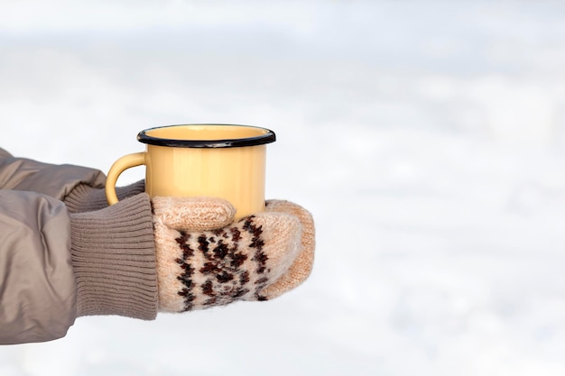 Cup of coffee in hands in gloves Female hands in mittens holding cup with hot coffee or tea