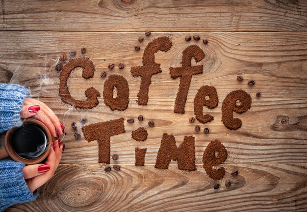 Cup of coffee in hands on textured wooden background.