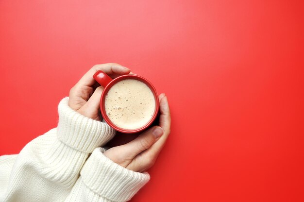 A cup of coffee in the hands of a woman on a red background