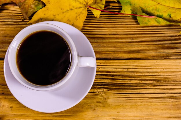 Photo cup of coffee and heap of yellow maple leaves on a wooden table top view