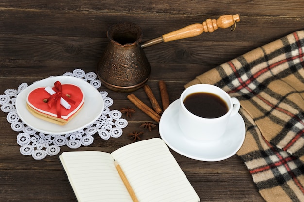 Чашка кофе, печенье в форме сердца с сообщением, блокнот, карандаш и кофейники