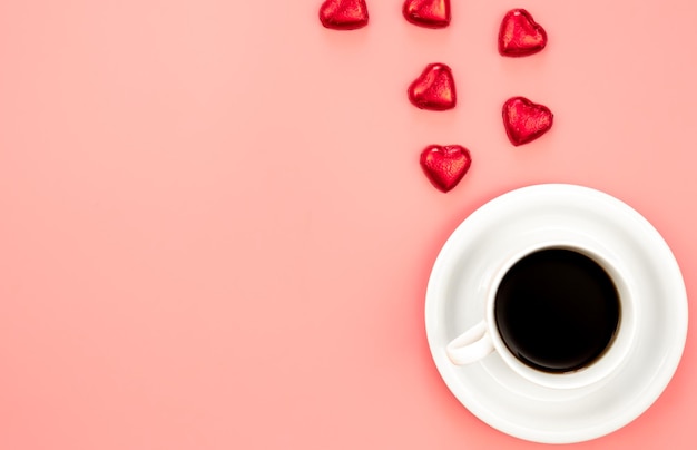 Cup of coffee and heart shaped sweets on a pink background flat lay