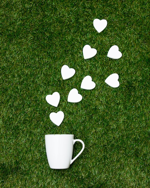 Cup of coffee and heart shapes on green grass.