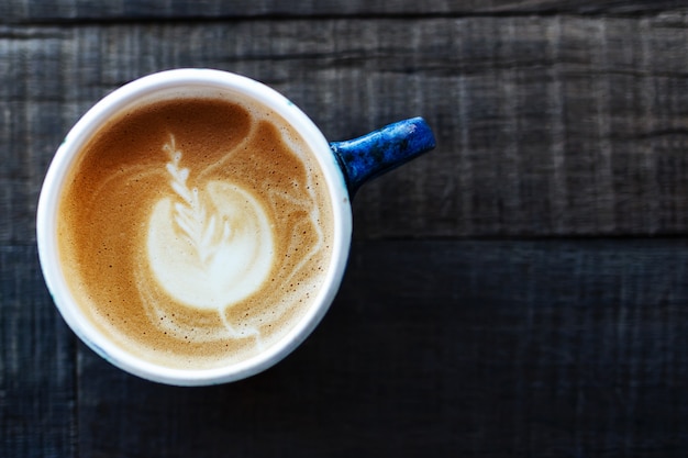 A cup of coffee is capped in a blue cup on a wooden background