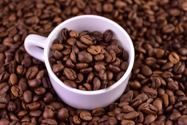 A cup of coffee is surrounded by a pile of coffee beans