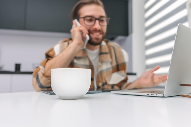 携帯電話で話している男性を背景に、テーブルの上にコーヒーが置かれている