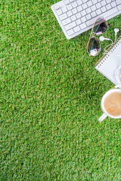 cup of coffee, keyboard, notebook on green grass
