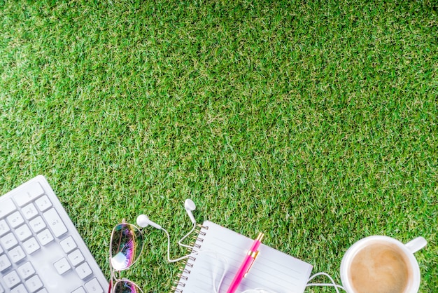 cup of coffee, keyboard, notebook on green grass