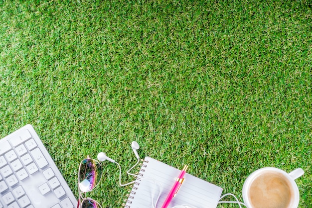 Cup of coffee, keyboard, notebook on green grass