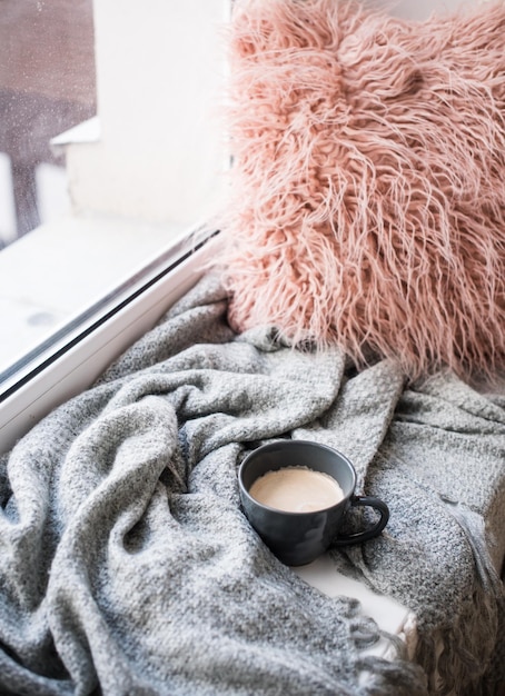 Foto coperta lavorata a maglia con tazza di caffè e soffice cuscino sul davanzale accogliente