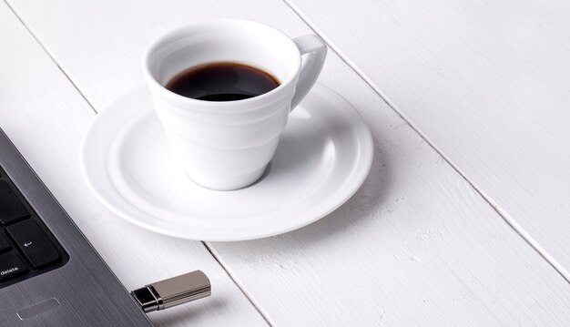 The cup of coffee and laptop on the white wooden table