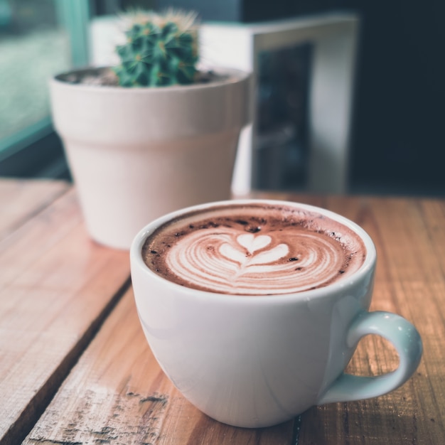 A cup of coffee latte art with heart in a white cup with cactus 