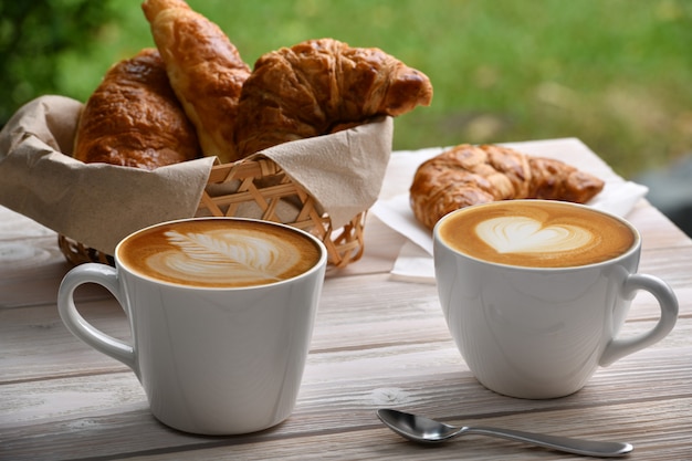 Cup of coffee latte and croissant on white wooden table