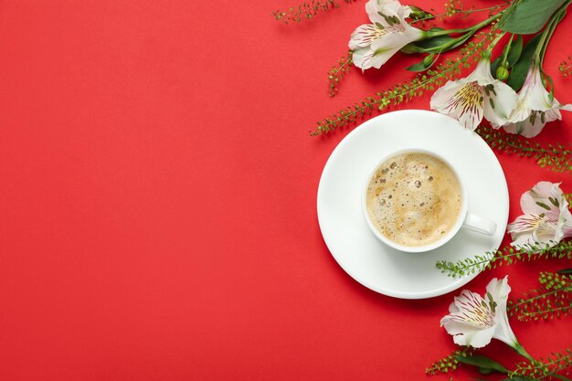 Cup of coffee and lilies on red background