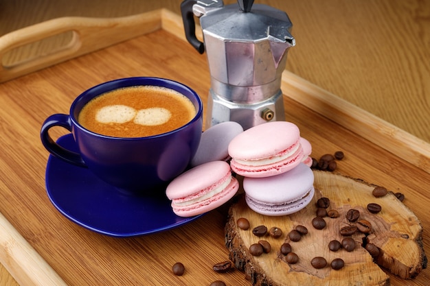 Tazza di amaretti e chicchi di caffè su un piatto da portata e caffettiera geyser su un vassoio di legno