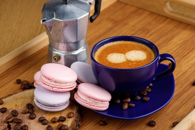 Cup of coffee macaroons and coffee beans on a platter and geyser coffee maker on a wooden tray