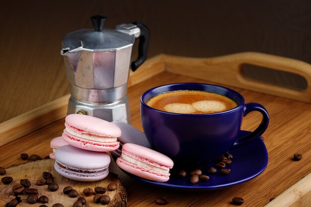 Cup of coffee macaroons and coffee beans on a platter and geyser coffee maker on a wooden tray