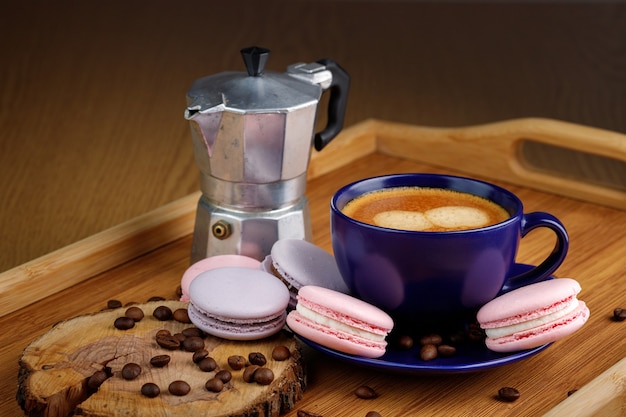 Cup of coffee macaroons and coffee beans on a platter and geyser coffee maker on a wooden tray