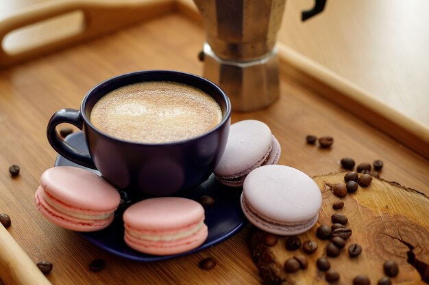 Cup of coffee macaroons and coffee beans on a platter on a wooden tray