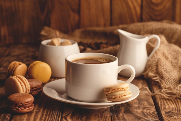 Cup of coffee milk sugar and macaroons on wooden background