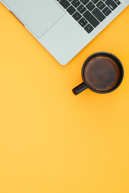 Cup of coffee and a modern notebook are isolated on a orange surface