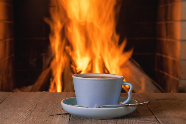 Cup of coffee near cozy fireplace background .