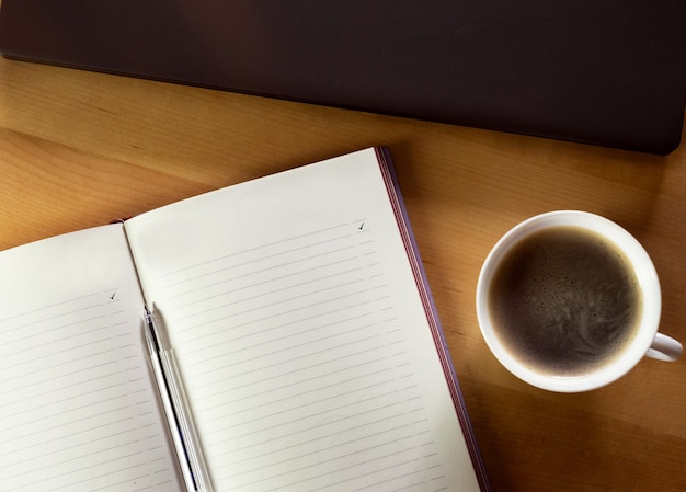 A cup of coffee, a notebook and a laptop on a wooden table.