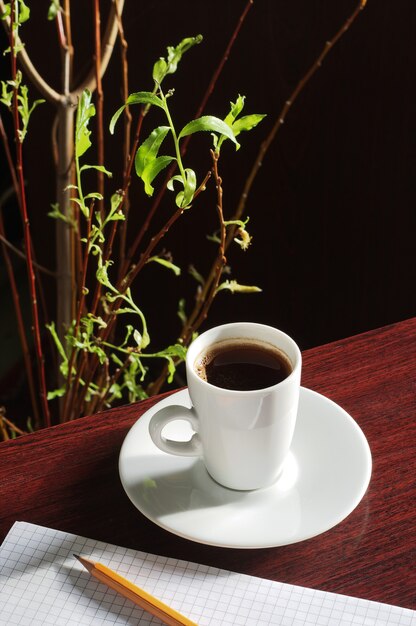 Чашка кофе и блокнот на деревянном столе в солнечном свете