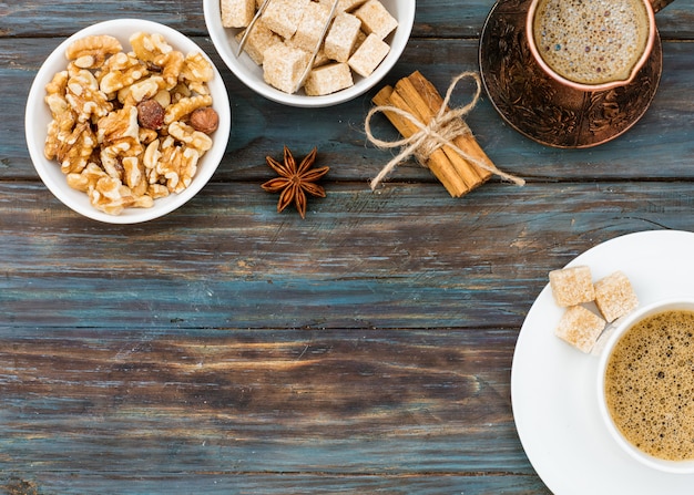 Cup of coffee, nuts in the bowl, coffeepot, cinnamon, anise, sugar, coffee beans on a wooden background