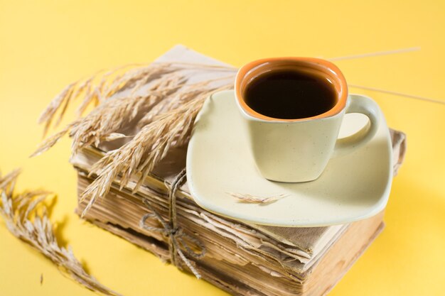 A cup of coffee on old books and dry ears of corn in yellow and harsh light. Wellness, harmony, inclusiveness