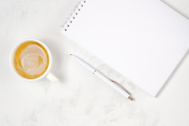 Cup of coffee, open notebook and pen on a light concrete background. Workplace top view. Place for text