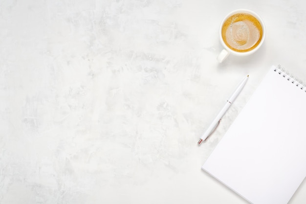 Cup of coffee, open notebook and pen on a light concrete background. Workplace top view. Place for text