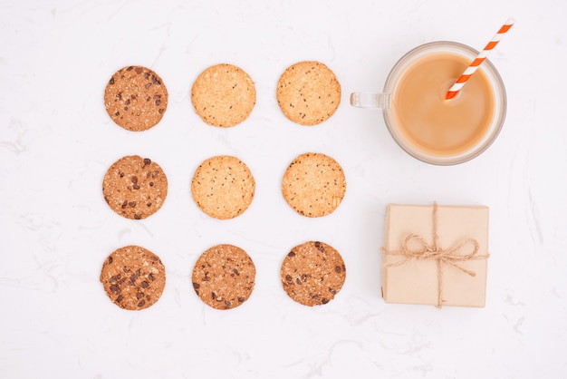 Cup of coffee among pattern of various shortbread and oat cookies with cereals and raisin on black wooden background. Top view, flat lay.