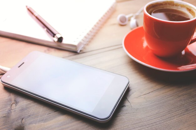 Cup of coffee, phone, earphone, notebook and pen on wooden table