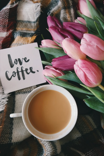 A cup of coffee on a plaid plaid along with tulips and a greeting card