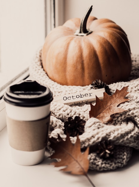 Tazza di caffè, zucca, foglie di autunno secche sulla finestra.