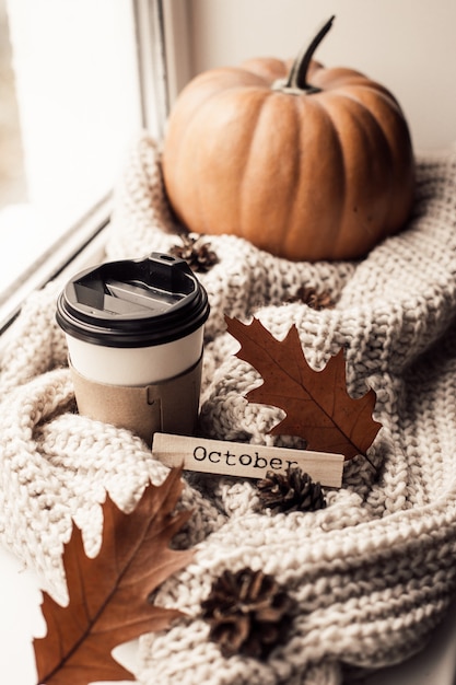 Photo cup of coffee, pumpkin, dried autumn leaves on window.