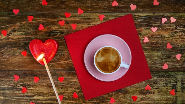 Cup of coffee on red napkin and set fire heart-shaped candle with long match. A romantic day.