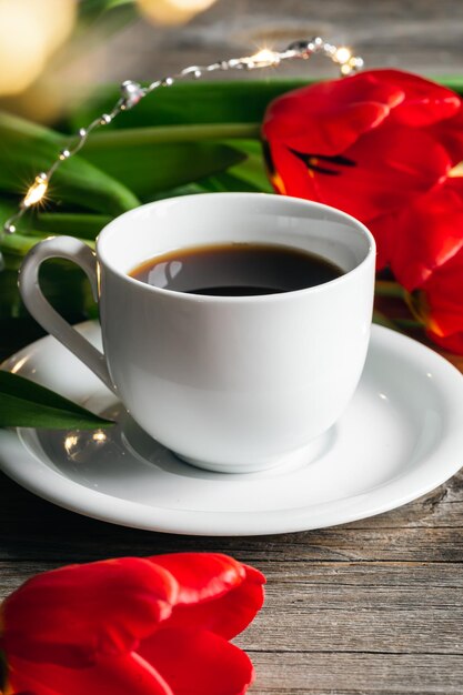 Cup of coffee and red tulips on a wooden surface