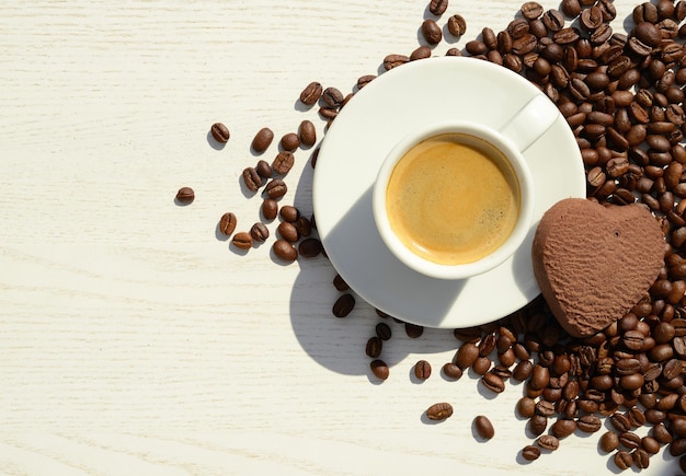 Cup of coffee roasted coffee beans heart shaped cookie white wooden background copy space flat lay