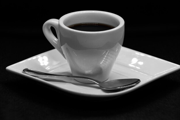 Cup of coffee on saucer and spoon on black background.