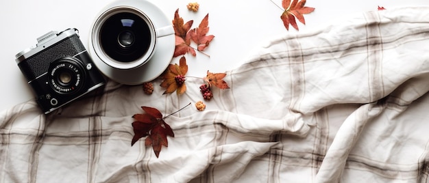 A cup of coffee sits on a blanket with autumn leaves on it.