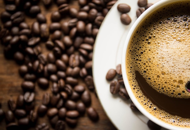 A cup of coffee sits on a plate next to coffee beans.