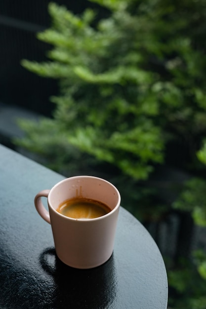 A cup of coffee sits on a table in front of a tree.