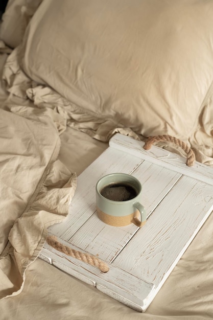 A cup of coffee sits on a tray on a bed.