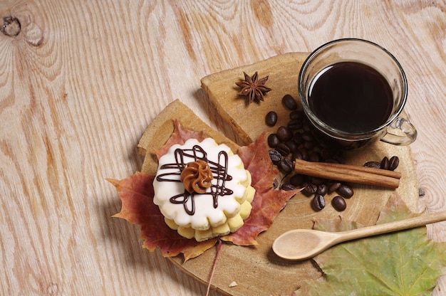 一杯のコーヒー、小さな丸いケーキ、古い木製のテーブルに紅葉